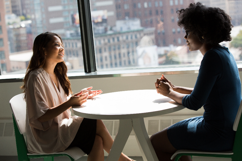 Two people in conversation across a table beside a window